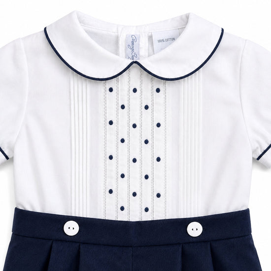 Carriage Boutique baby bobbie suit featuring a white shirt with navy pintucks, dot embroidery, and navy piping details.