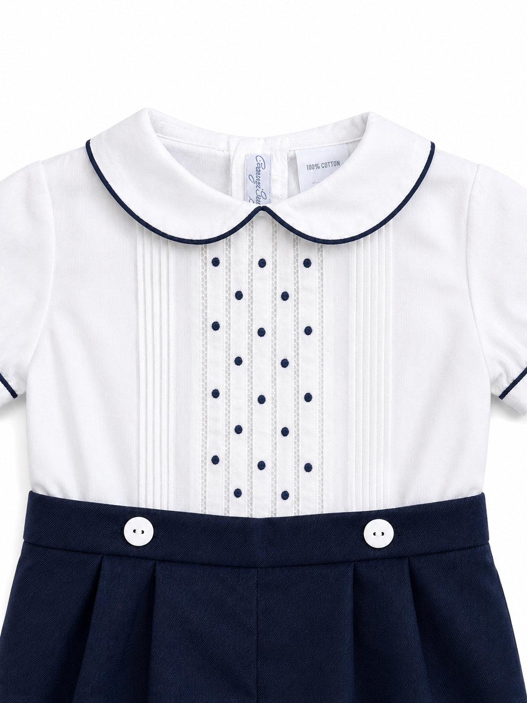 Carriage Boutique baby bobbie suit featuring a white shirt with navy pintucks, dot embroidery, and navy piping details.