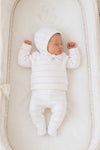Newborn baby sleeping in a Carriage Boutique white knit set with blush pink stripes, including leggings and a bonnet.