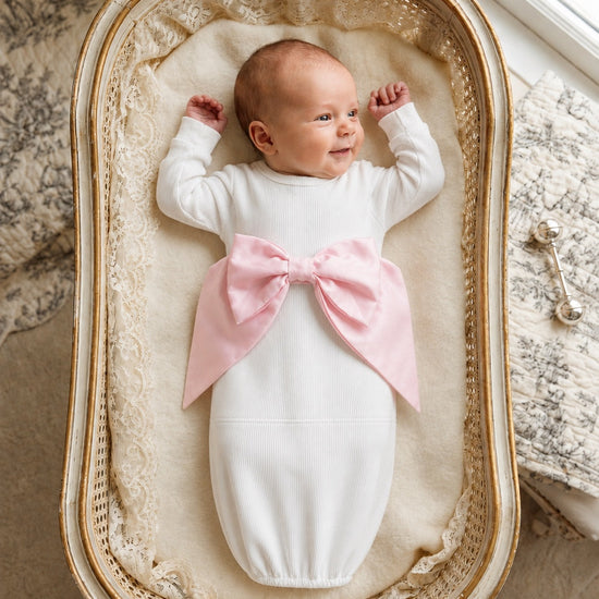 Carriage Boutique newborn baby girl in a white cotton swaddle bag featuring a large pink ribbon bow
