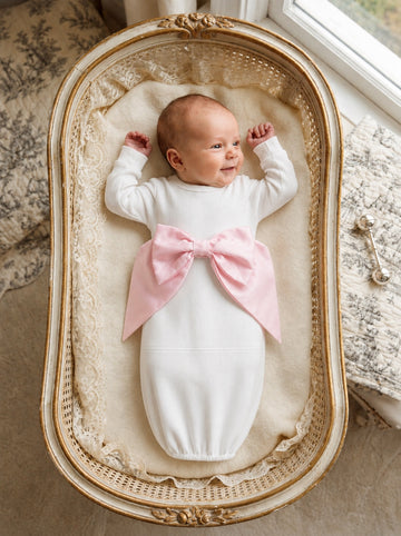 Carriage Boutique newborn baby girl in a white cotton swaddle bag featuring a large pink ribbon bow