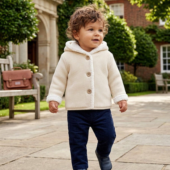 Toddler wearing a Carriage Boutique off-white knit cotton hooded jacket with sherpa lining and front button closure.