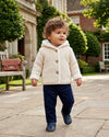 Toddler wearing a Carriage Boutique off-white knit cotton hooded jacket with sherpa lining and front button closure.