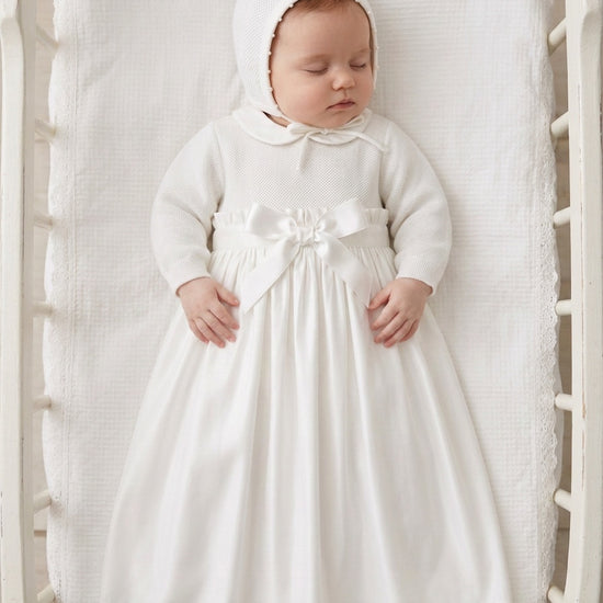 Carriage Boutique baby girl christening gown in white with pebble stitch texture, satin bow, and matching bonnet.