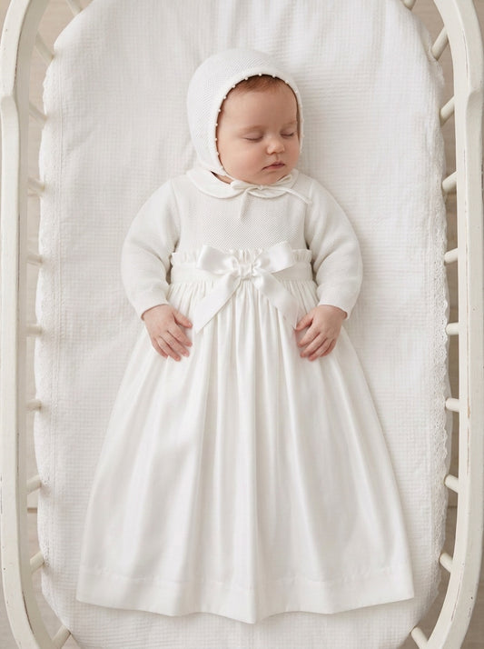Carriage Boutique baby girl christening gown in white with pebble stitch texture, satin bow, and matching bonnet.