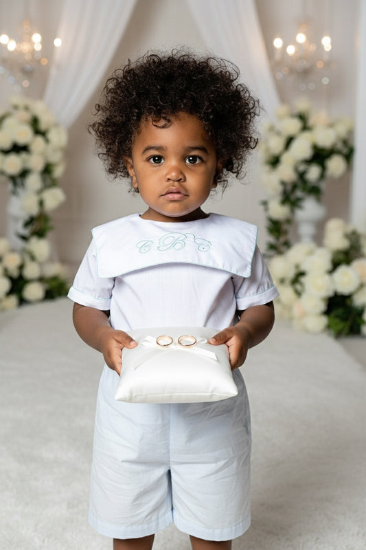 Carriage Boutique personalized white and blue cotton bobby suit worn by a toddler holding a ring bearer pillow
