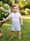Carriage Boutique personalized white and light blue cotton bobby suit worn by a toddler in a garden setting.