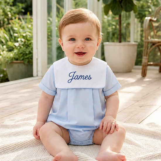 Carriage Boutique baby boy wearing a light blue cotton romper with a white collar and personalized name embroidery
