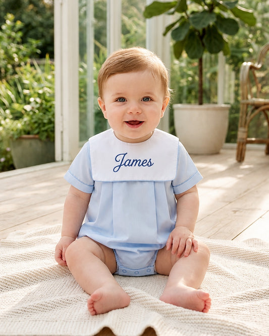 Carriage Boutique baby boy wearing a light blue cotton romper with a white collar and personalized name embroidery