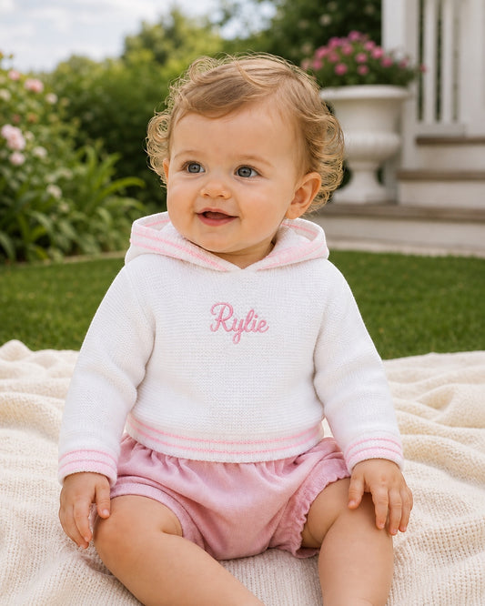 Carriage Boutique white hooded sweater with pink trim and personalized embroidery worn by a baby girl outdoors.