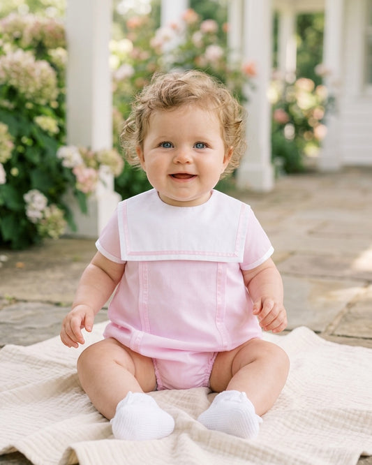 Carriage Boutique pink baby bubble romper with white Peter Pan collar worn by a smiling baby girl outdoors