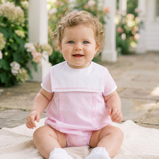 Carriage Boutique baby girl bubble romper in pink with a white Peter Pan collar, worn by a smiling baby outdoors.