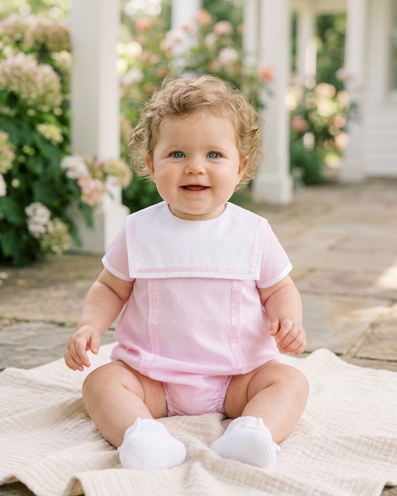 Carriage Boutique baby girl bubble romper in pink with a white Peter Pan collar, worn by a smiling baby outdoors.