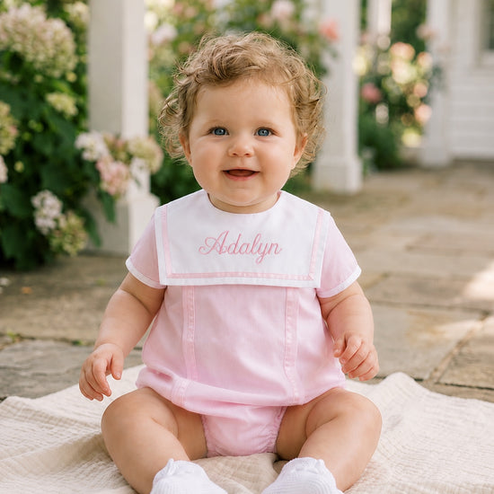 Carriage Boutique baby girl bubble romper in pink with white collar and personalized embroidery sitting on a blanket