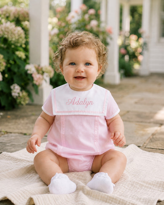 Carriage Boutique baby girl bubble romper in pink with white collar and personalized embroidery sitting on a blanket