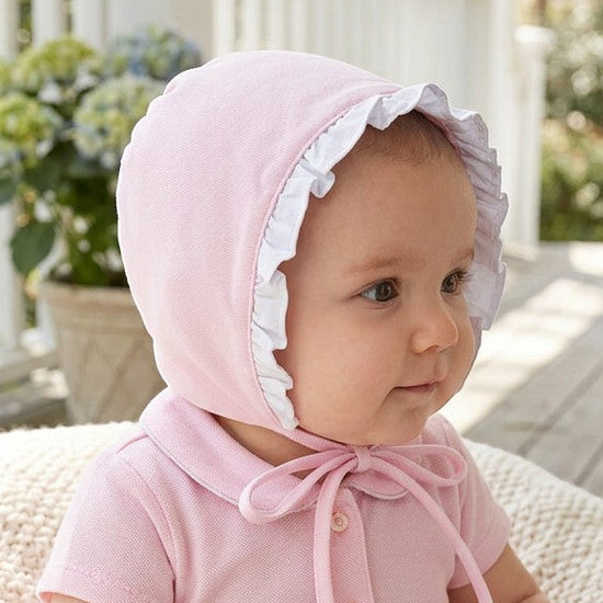 Carriage Boutique baby girl wearing a soft pink Easter shadow bonnet with white ruffled trim on a porch