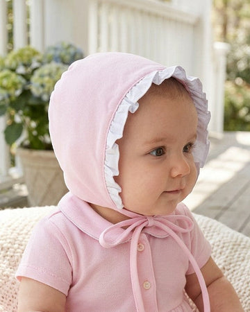 Carriage Boutique baby girl wearing a soft pink Easter shadow bonnet with white ruffled trim on a porch