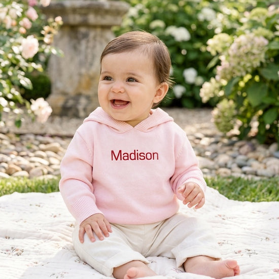 Carriage Boutique baby girl wearing a soft pink cotton knit sweater with a personalized name on a garden blanket.