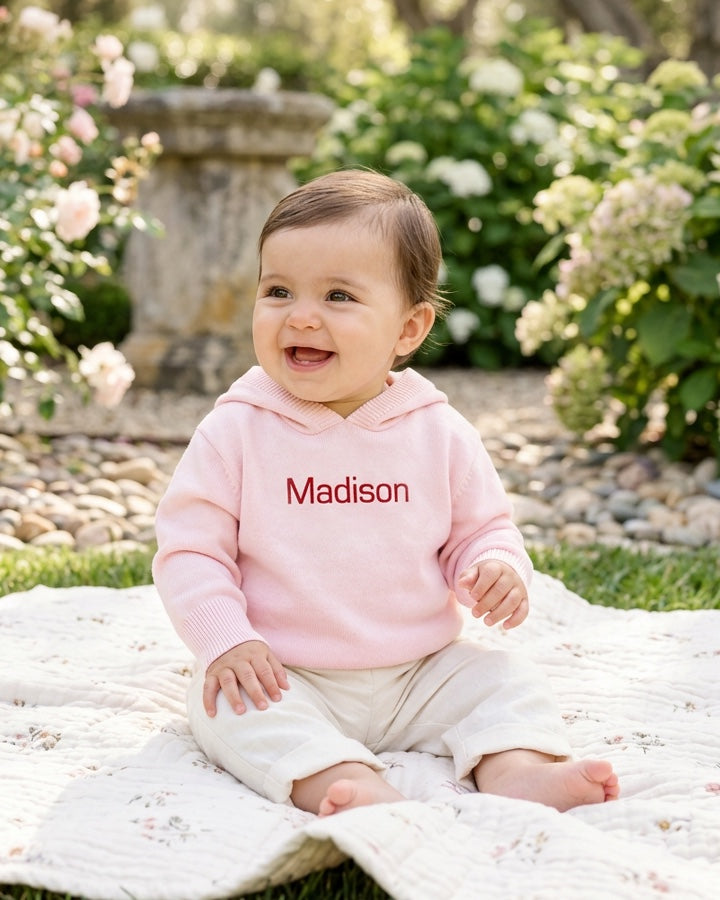 Carriage Boutique baby girl wearing a soft pink cotton knit sweater with a personalized name on a garden blanket.