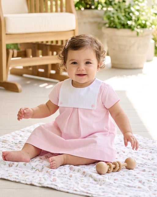 Baby girl wearing a Carriage Boutique personalized pink and white cotton dress with a button bib, sitting on a blanket