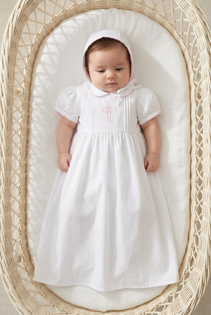 Carriage Boutique baby girl christening gown in white with pink embroidered cross and matching bonnet in a wicker bassinet