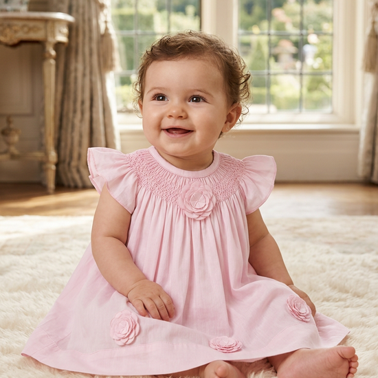 Carriage Boutique baby girl wearing a classic pink dress with smocked bodice and delicate cut-out flower details.