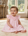 Carriage Boutique baby girl wearing a classic pink dress with smocked bodice and delicate cut-out flower details.