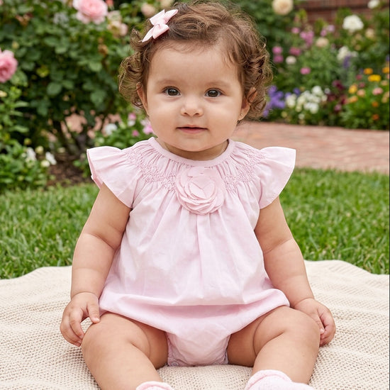 Carriage Boutique baby girl wearing a light pink bubble romper with ruffled sleeves and a large flower detail