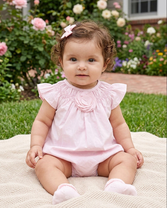 Carriage Boutique baby girl wearing a light pink bubble romper with ruffled sleeves and a large flower detail