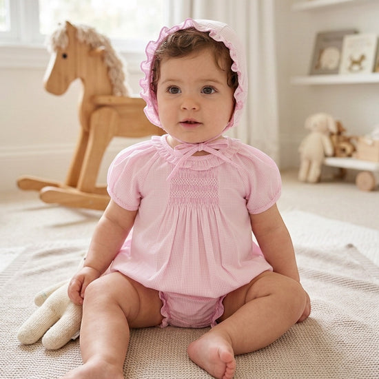 Baby girl wearing a pink gingham Carriage Boutique bubble romper with matching bonnet and hand-embroidered details.
