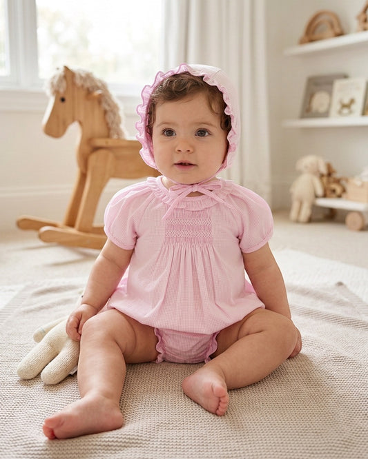 Baby girl wearing a pink gingham Carriage Boutique bubble romper with matching bonnet and hand-embroidered details.