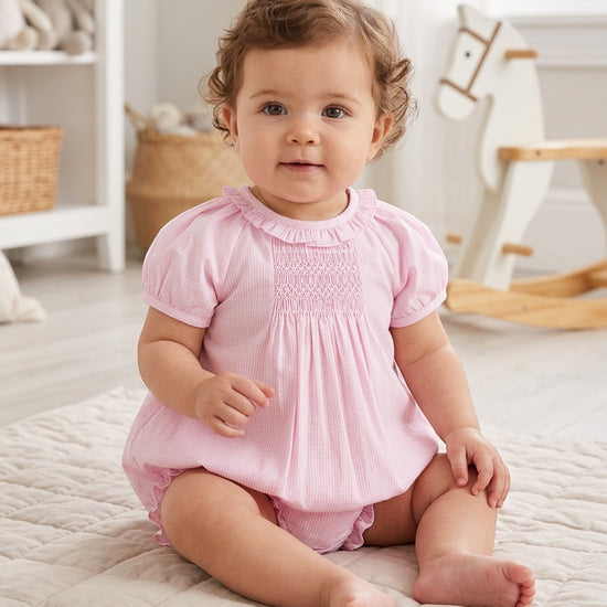 Carriage Boutique baby girl wearing a pink gingham cotton bubble romper with hand-embroidered smocking details.