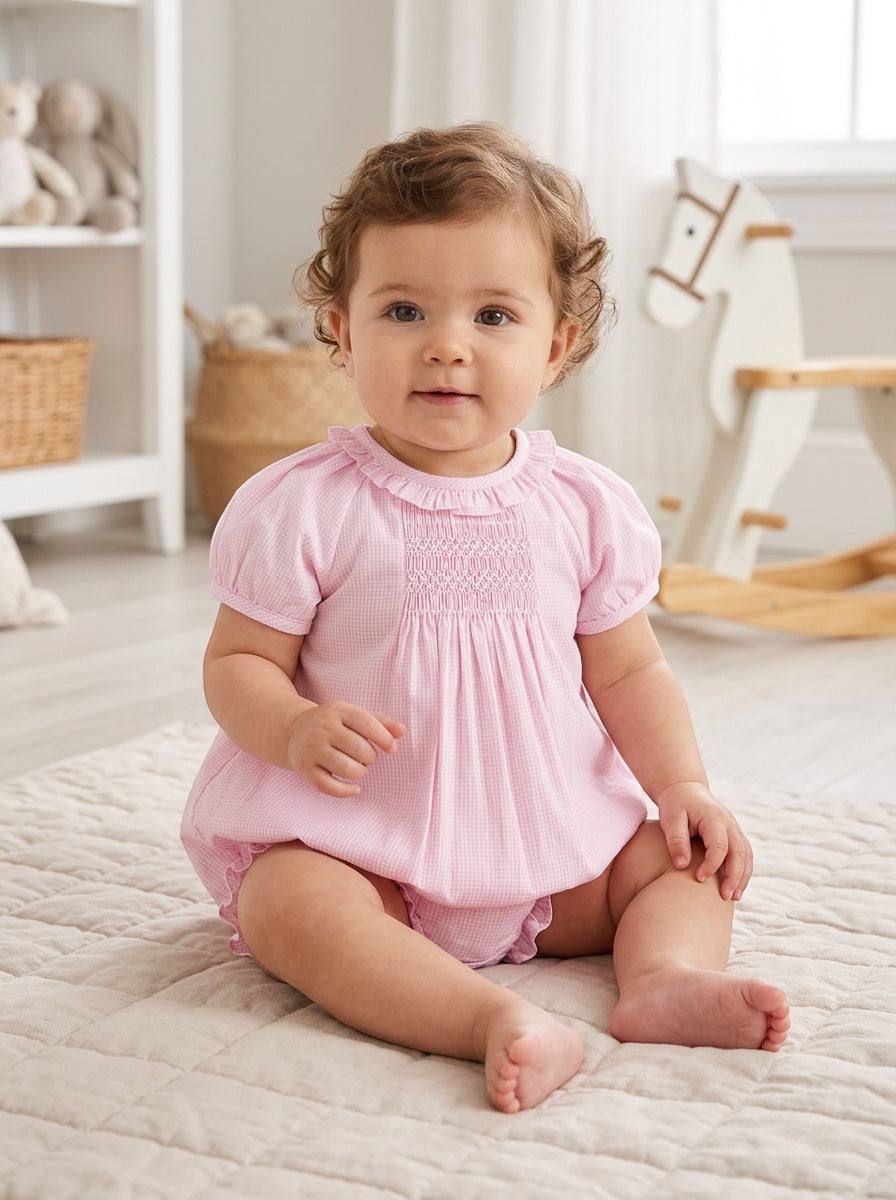 Carriage Boutique baby girl wearing a pink gingham cotton bubble romper with hand-embroidered smocking details.