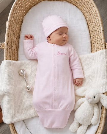 Carriage Boutique pink newborn sleep sack with matching hat and personalized name embroidery in a wicker bassinet.
