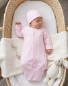 Carriage Boutique newborn pink sleep sack with matching hat, featuring scalloped trim and knotted bottom in a bassinet.
