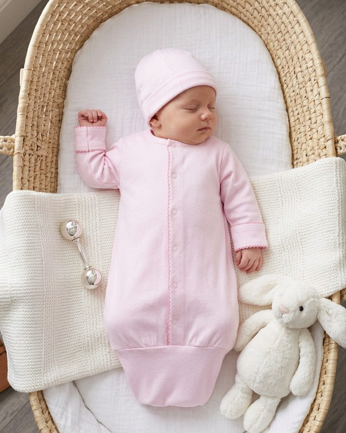 Carriage Boutique newborn pink sleep sack with matching hat, featuring scalloped trim and knotted bottom in a bassinet.
