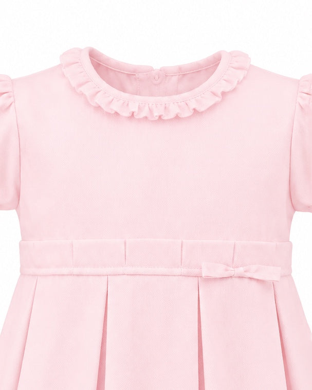 Carriage Boutique pink pique baby girl dress with a ruffled collar, pleated skirt, and delicate waist bow detail.