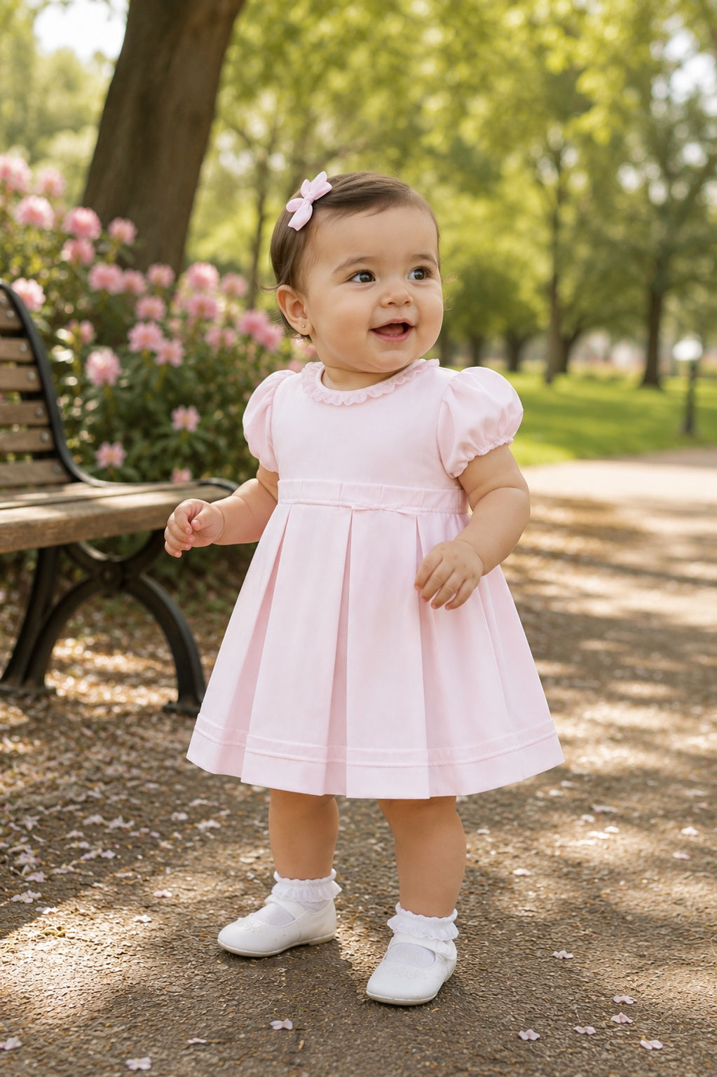 Carriage Boutique baby girl wearing a pink pique dress with puff sleeves and a matching bow headband in a park.