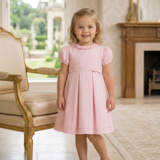 Carriage Boutique pink pique baby girl dress with ruffled collar and pleated skirt worn by a young girl indoors