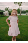 Carriage Boutique pink pique baby girl dress with ruffled collar, worn by a young girl in a grassy outdoor setting.