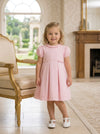 Carriage Boutique toddler girl wearing a pink pique dress with a ruffled collar and pleated skirt in a bright room