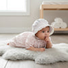 Carriage Boutique baby girl wearing a pink rosebud print cotton dress and matching lace-trimmed bonnet on a rug
