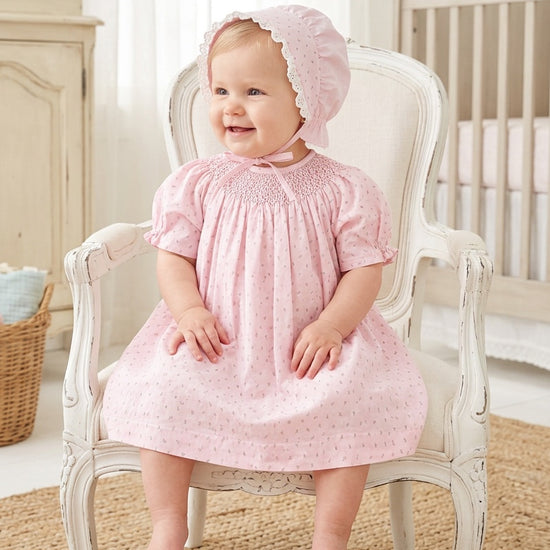 Carriage Boutique baby girl wearing a pink cotton dress with rosebud print and a matching lace-trimmed bonnet