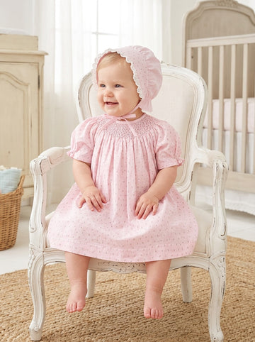 Carriage Boutique baby girl wearing a pink cotton dress with rosebud print and a matching lace-trimmed bonnet