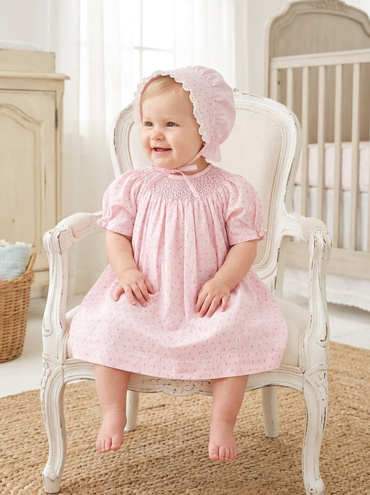 Carriage Boutique baby girl wearing a pink cotton dress with rosebud print and a matching lace-trimmed bonnet