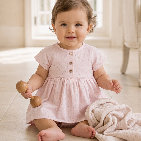 Carriage Boutique baby girl wearing a soft pink cotton dress with a rosebud print, wooden buttons, and puff sleeves.