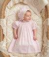 Carriage Boutique baby girl wearing a pink cotton dress with rosebud print and matching lace-trimmed bonnet in a basket