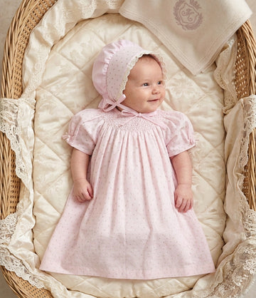 Carriage Boutique baby girl wearing a pink cotton dress with rosebud print and matching lace-trimmed bonnet in a basket