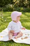 Carriage Boutique baby girl pink seersucker sun hat with chin tie worn by a baby sitting on a blanket in a garden