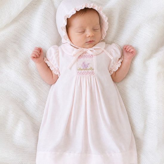 Sleeping baby in a Carriage Boutique pale pink smocked heirloom dress with bird embroidery and matching ruffled bonnet.